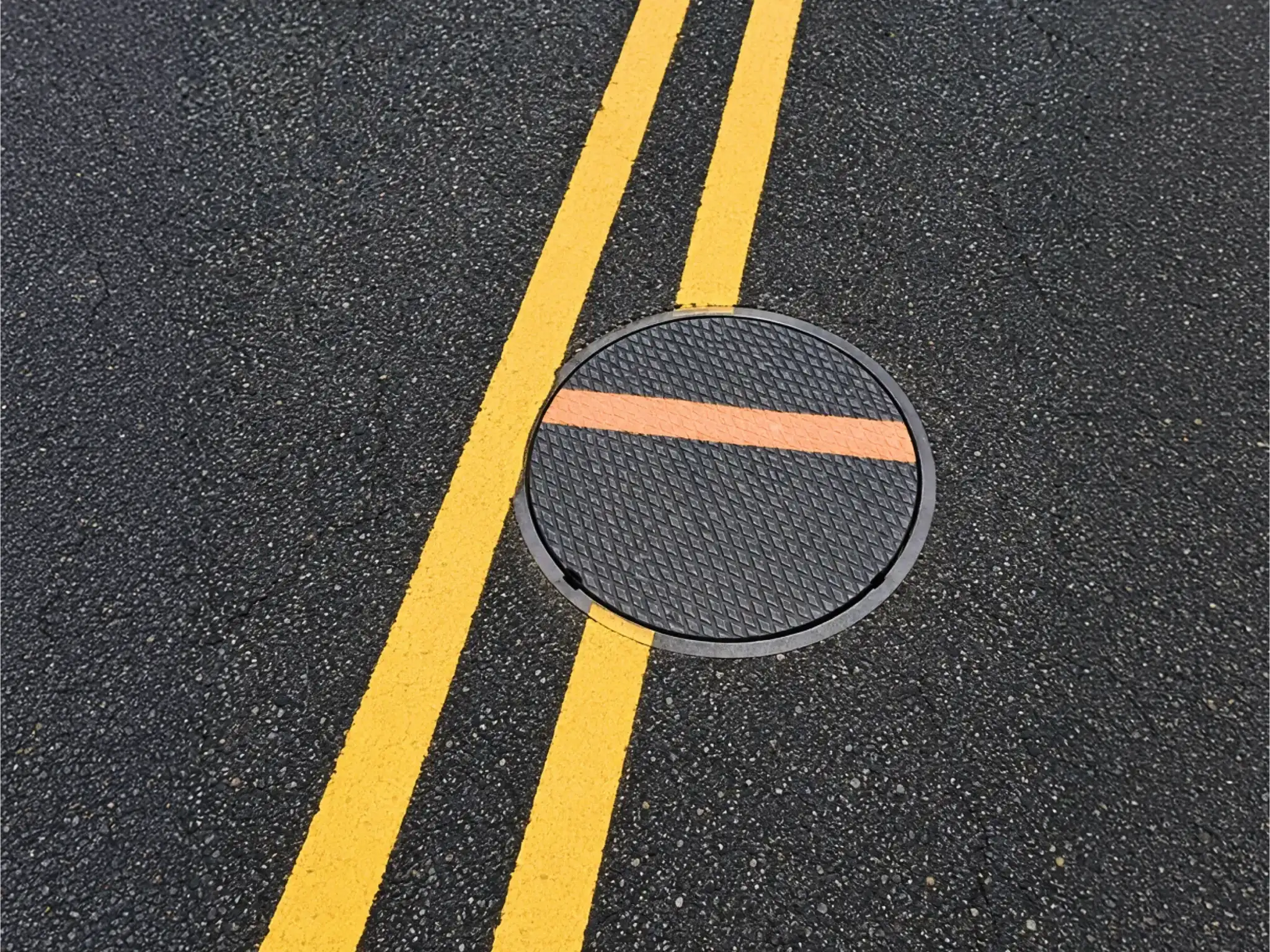 Yellow road lines and a manhole cover seen from above